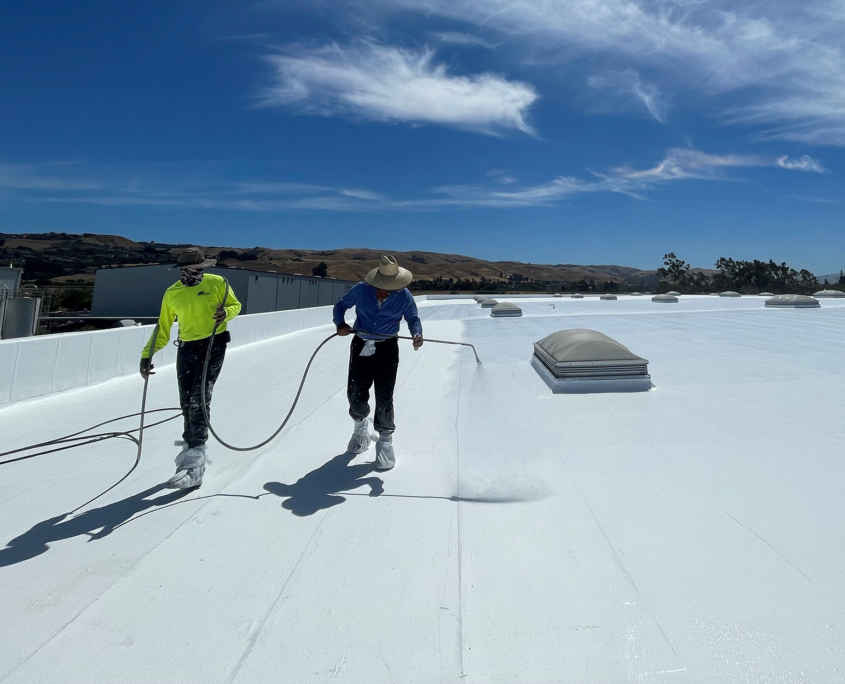 Two Workers Spraying Protective Coating On Roof