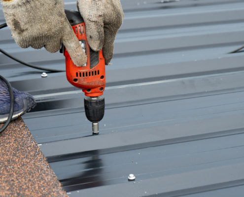 Workers Installing The Metal Sheet Roof By Electrical Drilling Machine