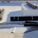 Rolls of white TPO and black EPDM roofing membrane staged on a commercial flat roof alongside metal fastening strips during installation