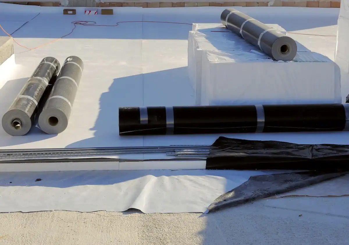 TPO and black EPDM roofing membrane Rolls of white TPO and black EPDM roofing membrane staged on a commercial flat roof alongside metal fastening strips during installation